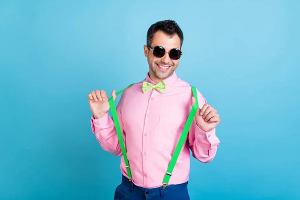 Foto von jungen hübschen Kerl glücklich positives Lächeln ziehen Hosenträger tragen Brille isoliert über blauer Farbe Hintergrund — Stockfoto