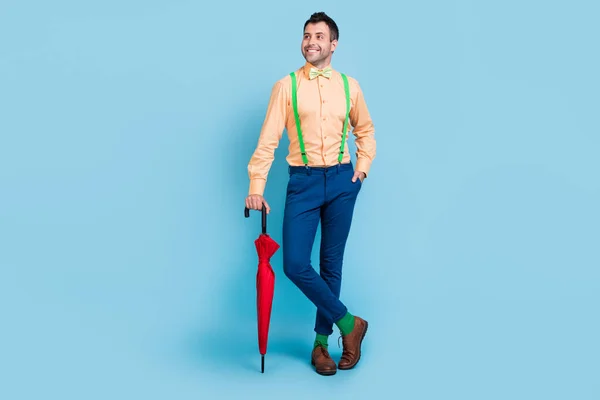 Photo of cheerful guy hold parasol look empty space wear suspenders shirt bow tie isolated blue color background — Stock Photo, Image