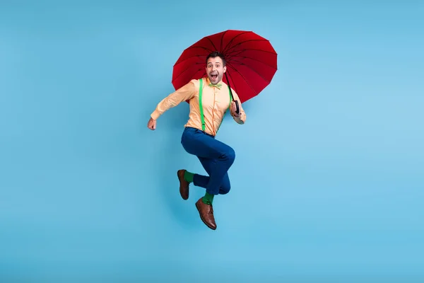 Ganzes Foto von lustigen brünetten Mann springen mit Sonnenschirm tragen Hemd Hose Socken Schuhe isoliert auf blauem Hintergrund — Stockfoto