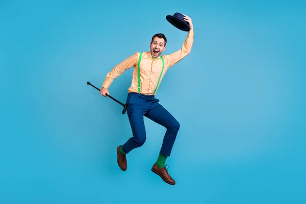 Foto de buen tipo salto llevar bastón sacar sombrero boca abierta desgaste tirantes camisa lazo aislado color azul fondo —  Fotos de Stock