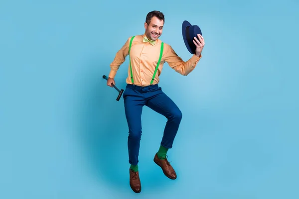 Foto de perfil de chico alegre salto mantenga la caña quitarse el sombrero usar tirantes camisa lazo aislado color azul fondo — Foto de Stock