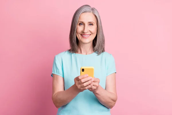 Foto de funky envelhecido penteado cinza senhora segurar telefone desgaste blusa teal isolado no fundo cor-de-rosa — Fotografia de Stock