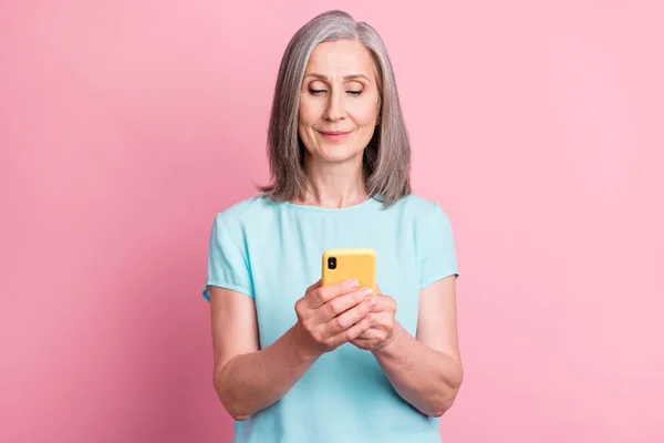 Foto di bella anziana capelli grigi signora sguardo telefono usura camicetta teal isolato su sfondo di colore rosa — Foto Stock