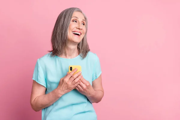 Foto di impressionato vecchi capelli bianchi signora tenere telefono sguardo vuoto spazio usura camicetta teal isolato su sfondo di colore rosa — Foto Stock