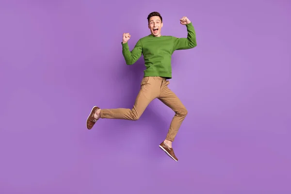 フルサイズ写真の若いですクールなブルネット男ジャンプ着用セーターパンツスニーカー隔離された紫色の背景 — ストック写真