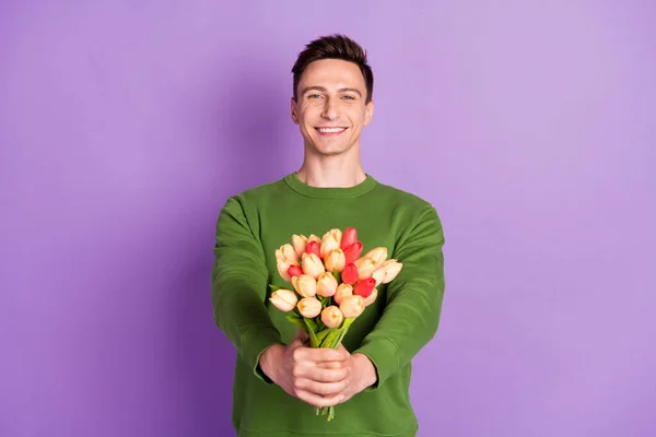 Foto van jonge flirterige brunet guy geven bloemen dragen trui geïsoleerd op paarse achtergrond — Stockfoto