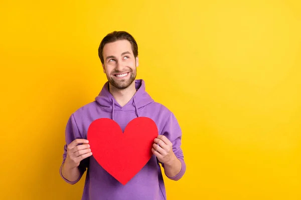 Fotografie mladého muže šťastný pozitivní úsměv držet červený papír srdce Valentýna sen izolované přes žluté barvy pozadí — Stock fotografie