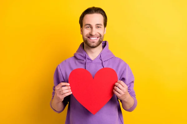 Photo of young guy happy positive smile hold red paper heart love feelings isolated over yellow color background — Stock Photo, Image