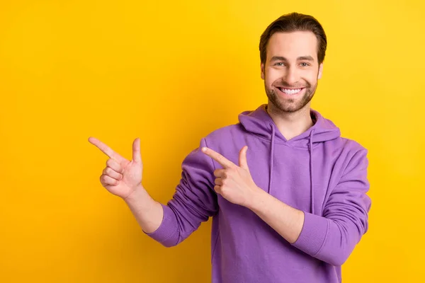 Foto von fröhlichen Kerl zeigen Zeigefinger leeren Raum fördern Verkauf tragen violetten Kapuzenpullover isoliert gelbe Farbe Hintergrund — Stockfoto