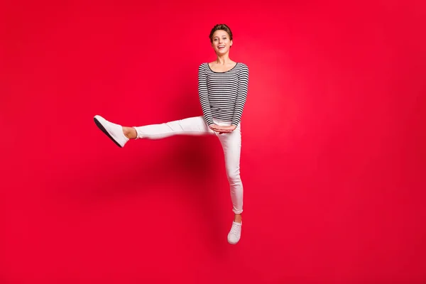 Фото чарівної красивої молодої леді носити смугастий одяг, посміхаючись стрибаючи високий ізольований фон червоного кольору — стокове фото