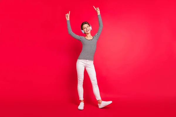 Bild av charmig söt kvinna klädd randig outfit hörlurar ler pekande fingrar tomt utrymme isolerad röd färg bakgrund — Stockfoto