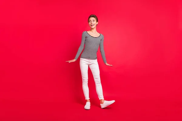 Foto de adorable dulce joven vestida a rayas traje sonriente buscando espacio vacío aislado color rojo fondo — Foto de Stock