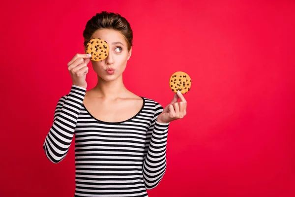 Foto de flerte bonita mulher vestida listrado roupa lábios despojado segurando cookies tampa olho vazio espaço isolado cor vermelha fundo — Fotografia de Stock