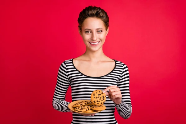 Foto de engraçado adorável jovem usar roupas listradas segurando placa de biscoito sorrindo isolado fundo cor vermelha — Fotografia de Stock