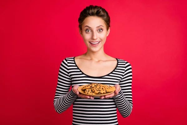 Foto de impressionado engraçado jovem usar roupas listradas segurando placa de biscoito sorrindo isolado fundo cor vermelha — Fotografia de Stock