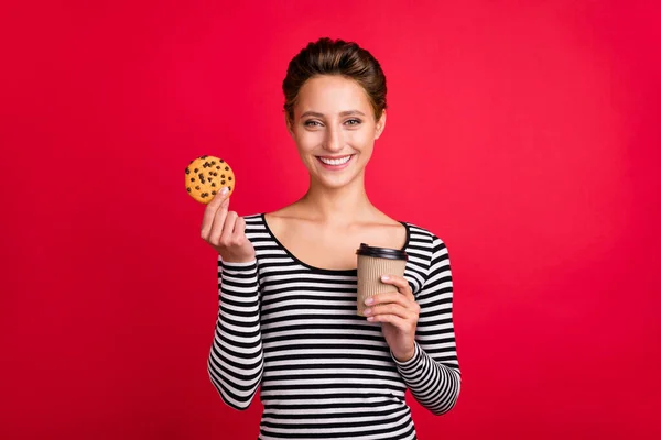 Fénykép bájos csinos fiatal nő öltözött csíkos ruhát gazdaság kávéscsésze mazsola cookie izolált piros színű háttér — Stock Fotó