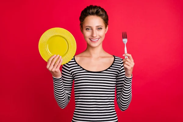 Foto wanita muda yang lapar mengenakan pakaian bergaris memegang garpu piring tersenyum latar belakang warna merah terisolasi — Stok Foto