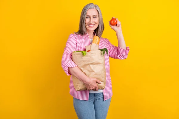 Foto van een oudere vrouw gelukkig positieve glimlach kopen voedsel zak houden tomaten organische eco geïsoleerd over gele kleur achtergrond — Stockfoto