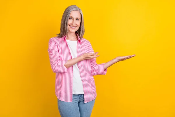 Bild av åldrade kvinna glad positiv leende visa händer produkt promo erbjudande försäljning isolerad över gul färg bakgrund — Stockfoto