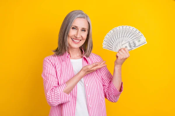 Photo de femme âgée heureux sourire positif montrer main argent cash dollars riche isolé sur fond de couleur jaune — Photo