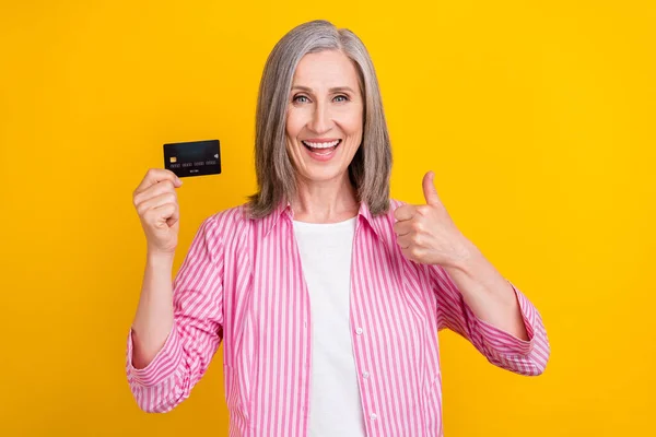 Foto da mulher idosa feliz sorriso positivo mostrar polegar-se como cartão de crédito anúncio fino isolado sobre fundo de cor amarela — Fotografia de Stock