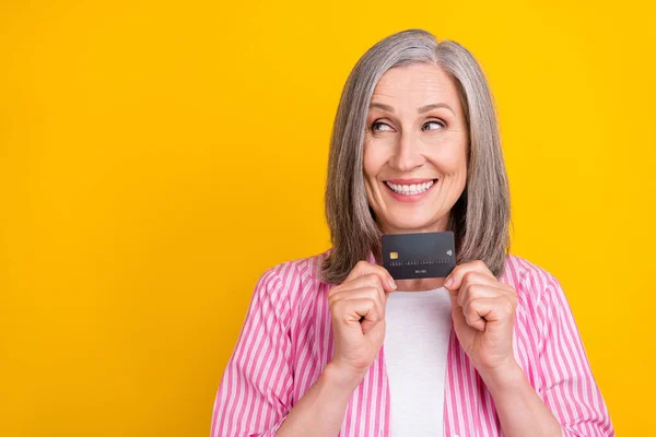 Foto von gealterten Frau glücklich positives Lächeln neugierig aussehen leeren Raum Kreditkarte Geld isoliert über gelben Farbhintergrund — Stockfoto