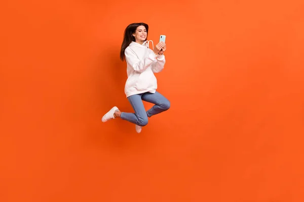 Full längd kroppsstorlek bild av ganska trendiga glada flicka hoppa med hjälp av enhet 5g isolerad över ljusa orange färg bakgrund — Stockfoto