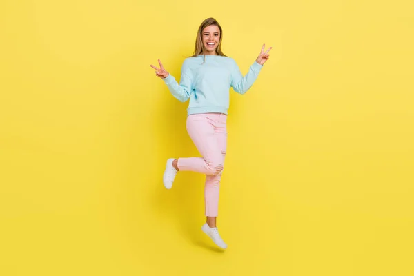 Повнометражний вигляд тіла привабливої веселої дівчини, що стрибає, показуючи v-знак ізольовано на яскраво-жовтому кольоровому фоні — стокове фото