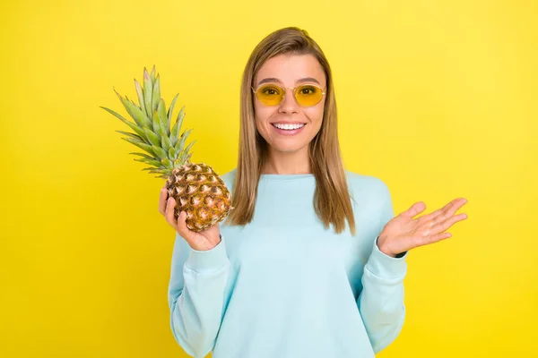 Zdjęcie uroczej blondynki trzymać świeży promień ananasa uśmiech nosić okulary przeciwsłoneczne niebieska koszula izolowane na żółtym tle — Zdjęcie stockowe