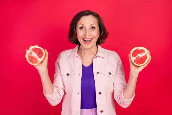 Foto von alten erstaunt Dame halten zwei Grapefruit Scheibe omg Reaktion tragen rosa Jacke isoliert rote Farbe Hintergrund — Stockfoto