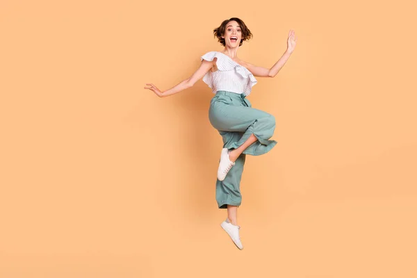 Foto de adorable mujer joven divertida vestida a rayas superior saltando alto aislado color beige fondo — Foto de Stock