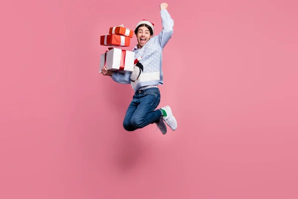 Foto de caballero afortunado salido usan suéter de año nuevo sonriendo saltando sosteniendo regalos levantando puño aislado color rosa fondo —  Fotos de Stock