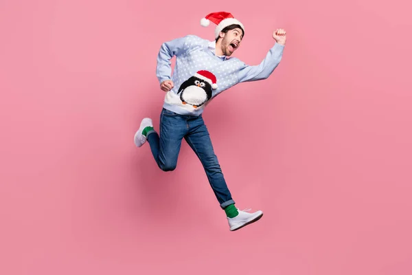 Φωτογραφία ενός πολύ γλυκού νεαρού άνδρα ντυμένος μπλε χριστουγεννιάτικο πουλόβερ τρέχει γρήγορα άλμα ψηλά χαμογελώντας απομονωμένο ροζ χρώμα φόντο — Φωτογραφία Αρχείου