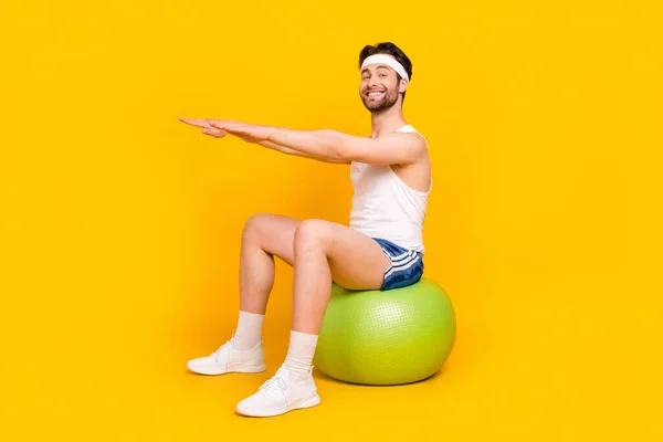 밝은 노란색 배경 위로 격리 된 채 공 위에 앉아 있는 매력적 인 남자의 전체 몸길이 프로필 — 스톡 사진
