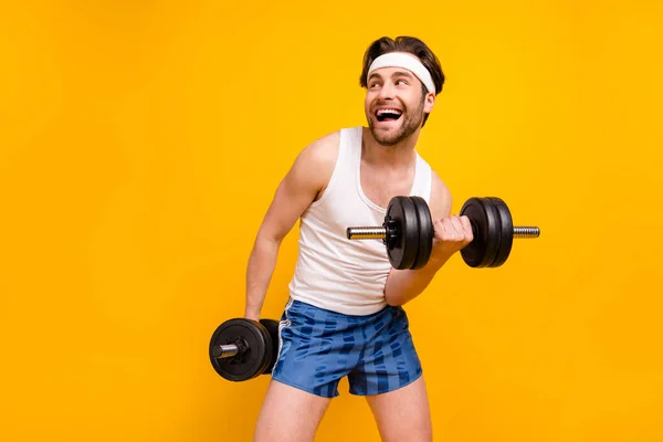 Портрет привлекательного веселого парня, поднимающего вес, работающего над активным увлечением, изолированным на ярко-желтом фоне — стоковое фото