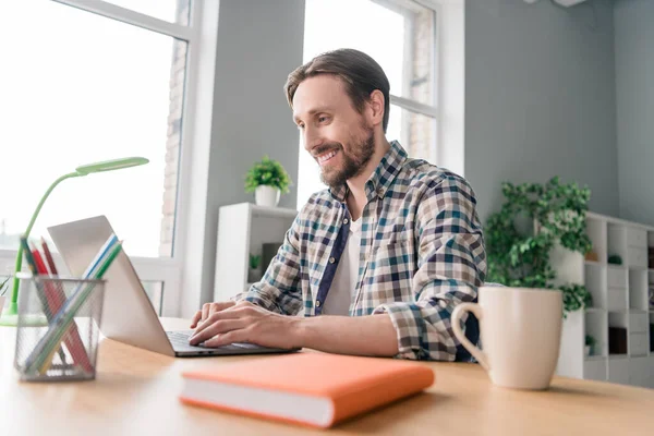 Foto van doordachte positieve volwassen man gekleed geruite shirt zittafel werken modern apparaat binnen appartement kantoor — Stockfoto