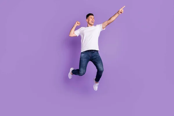 Full längd foto av glad ung glad man hoppa upp pekfingret tomt utrymme isolerad på lila färg bakgrund — Stockfoto