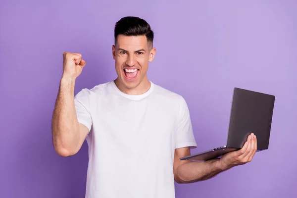 Фото молодого парня счастливой позитивной улыбкой провести ноутбук праздновать победу возбужден изолирован от фиолетового цвета фона — стоковое фото
