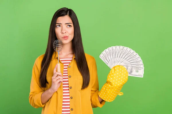 Photo de charmante douteuse jeune femme porter chemise jaune tenant ventilateur d'argent à la recherche d'espace vide isolé fond de couleur verte — Photo