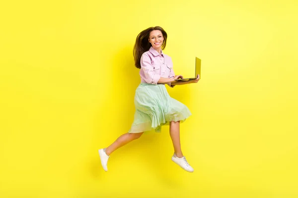 Tam boy vücut ölçüsü, parlak sarı arkaplan üzerinde izole edilmiş dizüstü bilgisayar kullanarak atlayan neşeli kız görüntüsü. — Stok fotoğraf
