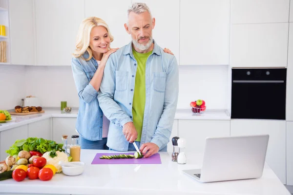 Foto av positiv gott humör stilig make titta på video i laptop förbereda frukost för fru klippa hacka gurka — Stockfoto