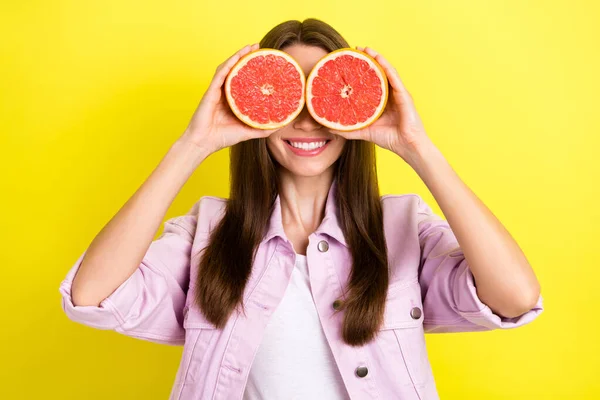 Foto retrato mujer joven cubriendo los ojos con dos mitades de pomelo juguetón aislado vibrante color amarillo fondo —  Fotos de Stock