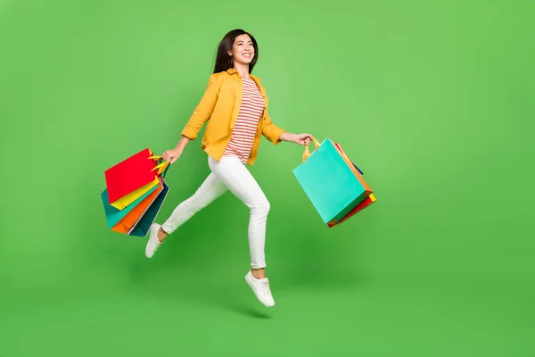Teljes méretű profil fotó édes barna frizura millenniumi hölgy tart táskák futtatni kopás nadrág cipők elszigetelt zöld színű háttér — Stock Fotó