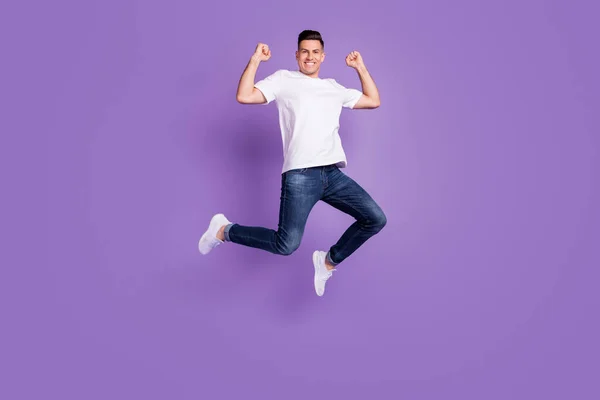 Полная длина фото молодого человека счастливая положительная улыбка прыжок вверх показать мышцы радуются победе изолированы над фиолетовым цветом фона — стоковое фото