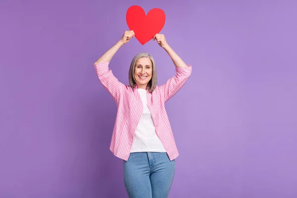 Foto de mujer anciana feliz sonrisa positiva celebrar papel rojo día de San Valentín corazón aislado sobre fondo de color violeta — Foto de Stock