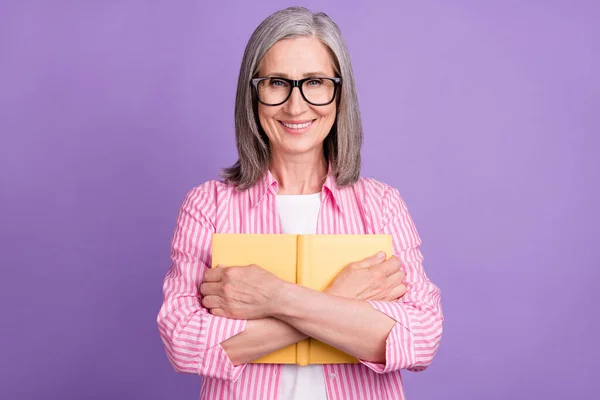 Mutlu gülümseyen yaşlı kadının fotoğrafı menekşe rengi arka planında izole edilmiş kitap okuyucu eğitimini kucakla — Stok fotoğraf