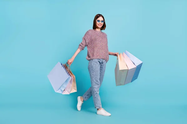 Foto de senhora positiva passo realizar pechinchas desgaste camisola de vidro solar jeans calçado isolado azul cor de fundo — Fotografia de Stock