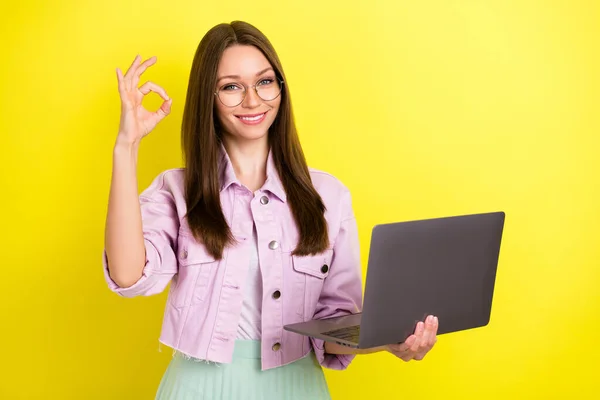 Retrato de especialista menina alegre atraente mostrando ok-sinal usando laptop isolado sobre fundo de cor amarela brilhante — Fotografia de Stock