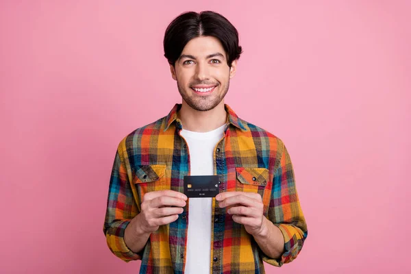 Foto de carismático muito jovem cavalheiro usar roupa xadrez segurando cartão de crédito sorrindo isolado cor de fundo rosa — Fotografia de Stock