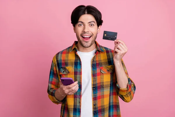 Foto van charmante zoete man gekleed geruite kleding typen moderne apparaat holding card geïsoleerde roze kleur achtergrond — Stockfoto